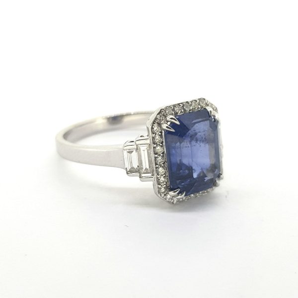 Sapphire and Diamond Cluster Ring; central 3.28ct emerald-shaped step-cut sapphire within a brilliant-cut diamond surround with baguette-cut diamonds at each shoulder