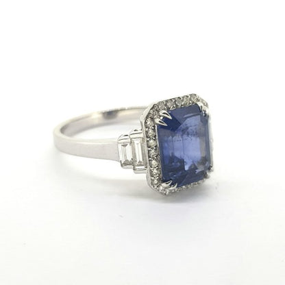 Sapphire and Diamond Cluster Ring; central 3.28ct emerald-shaped step-cut sapphire within a brilliant-cut diamond surround with baguette-cut diamonds at each shoulder