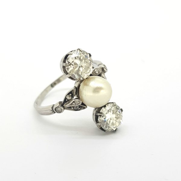 Natural Pearl and Old Cut Diamond Trilogy Ring; comprising a natural pearl set between two old cut diamonds, decorative diamond set shoulders open up in leaf form towards the pearl, 1.20 carats