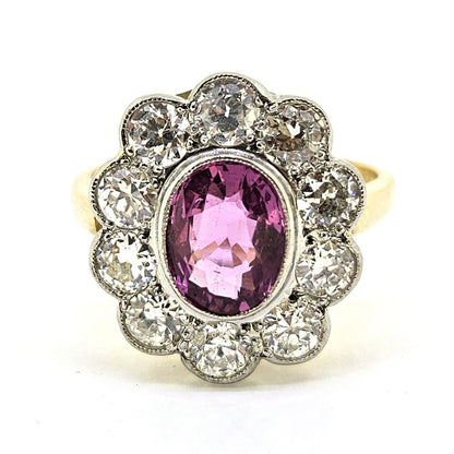 A pink sapphire and round diamond oval shaped cluster ring in yellow and white metal, on a white background