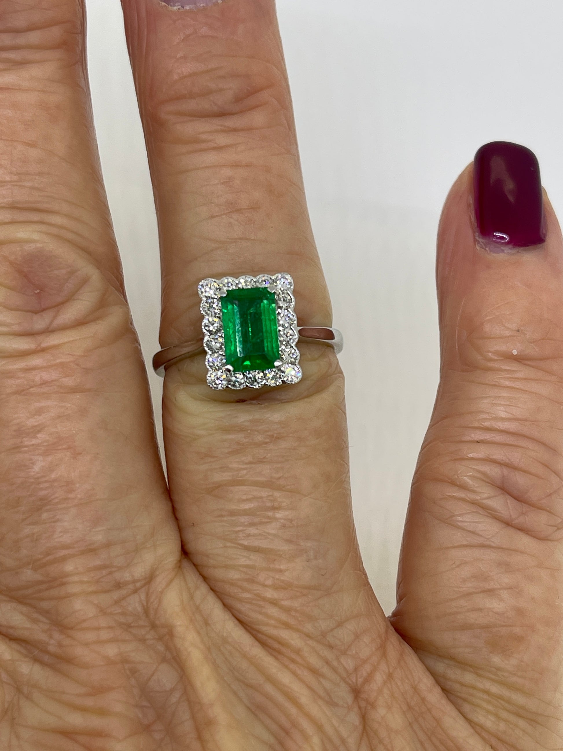 An emerald and diamond rectangular cluster ring in white gold, modelled on a ring finger