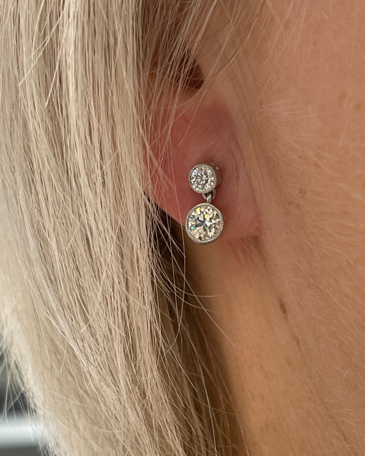 A round brilliant cut diamond double drop earring in white metal, modelled in an ear