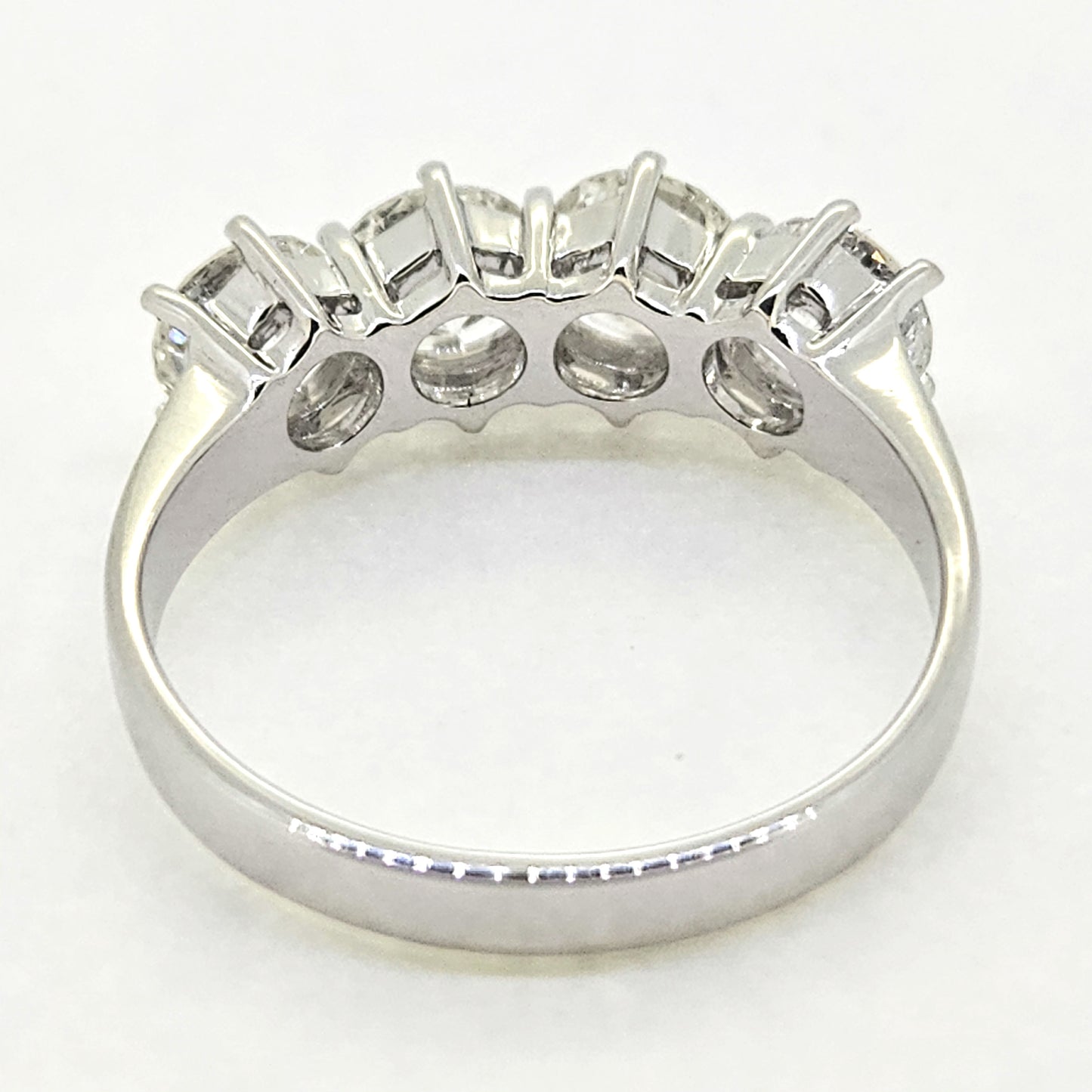 A four stone brilliant cut diamond ring in white gold, viewed from behind, on a white background