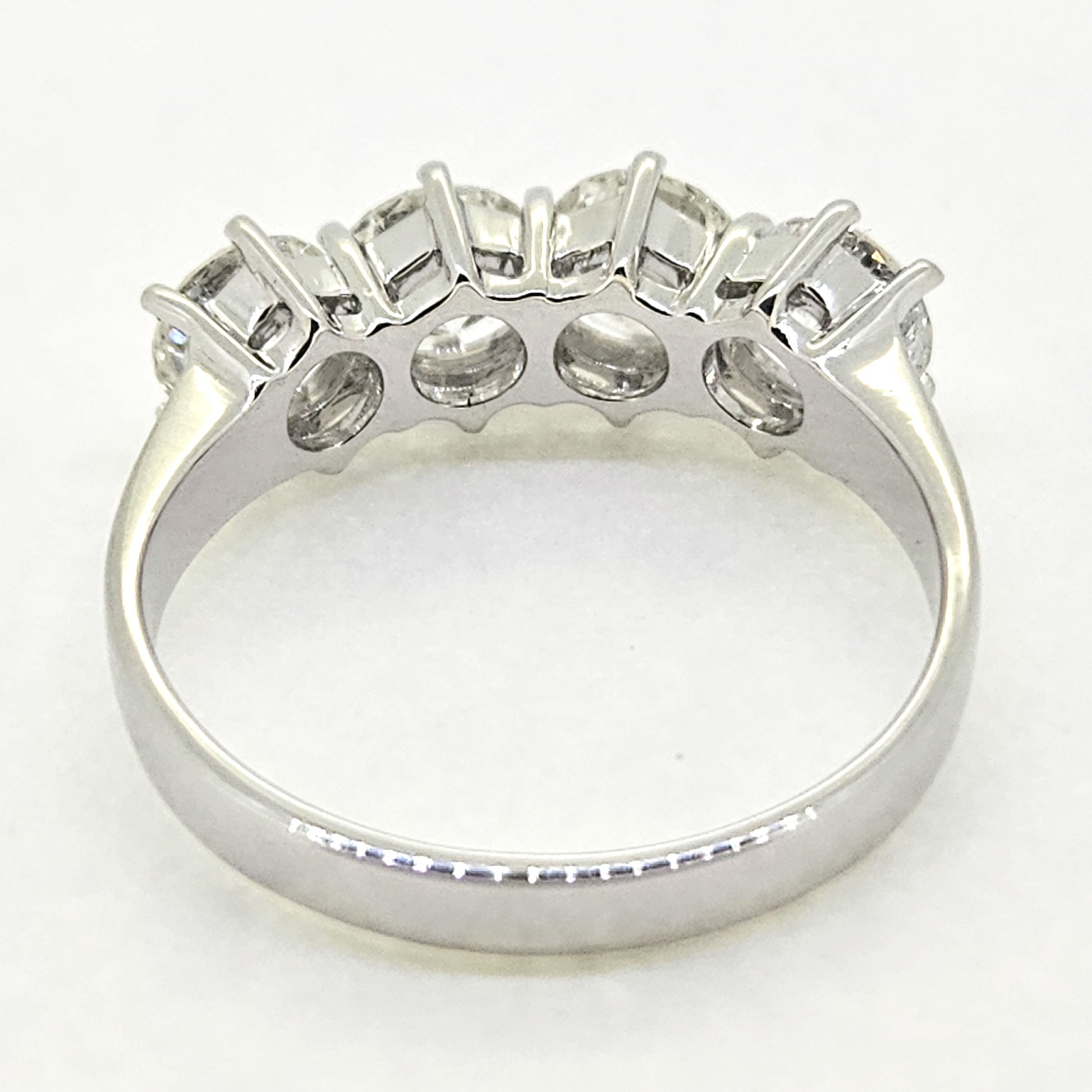 A four stone brilliant cut diamond ring in white gold, viewed from behind, on a white background