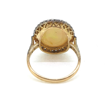 A cabochon opal and diamond oval cluster ring in gold and silver, viewed from behind, on a white background