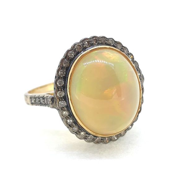 A cabochon opal and diamond oval cluster ring in gold and silver, on a white background