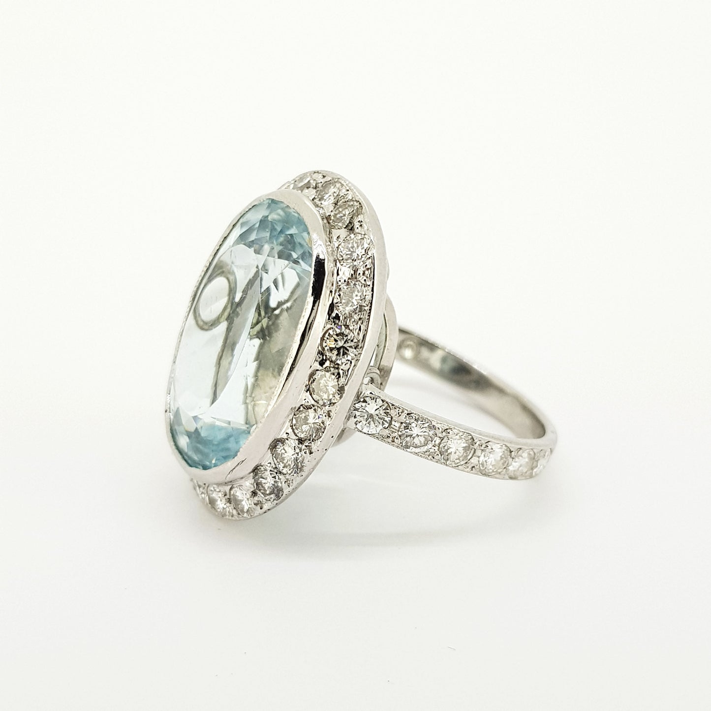 An aquamarine and diamond large oval cluster ring in white metal, against a white background
