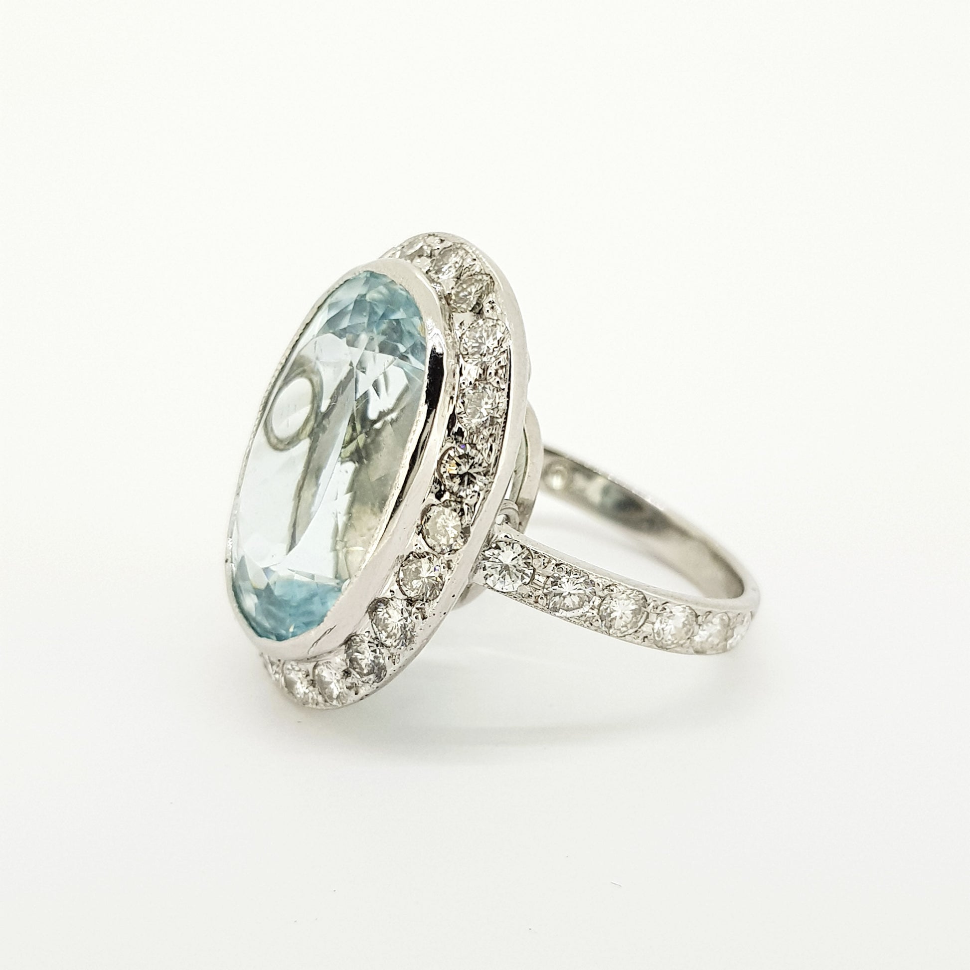 An aquamarine and diamond large oval cluster ring in white metal, against a white background