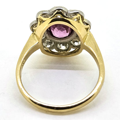 A pink sapphire and round diamond oval shaped cluster ring in yellow and white metal, on a white background