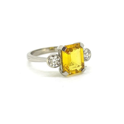 Yellow Sapphire and Diamond Three Stone Ring; central claw-set 2.80ct emerald-cut yellow sapphire flanked by 0.50cts collet-set round brilliant-cut diamonds, in 18ct white gold
