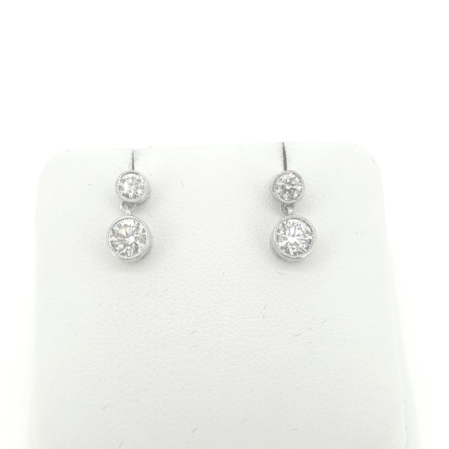 A pair of round brilliant cut diamond double drop earrings in white metal, on an earring display pad, on a white background