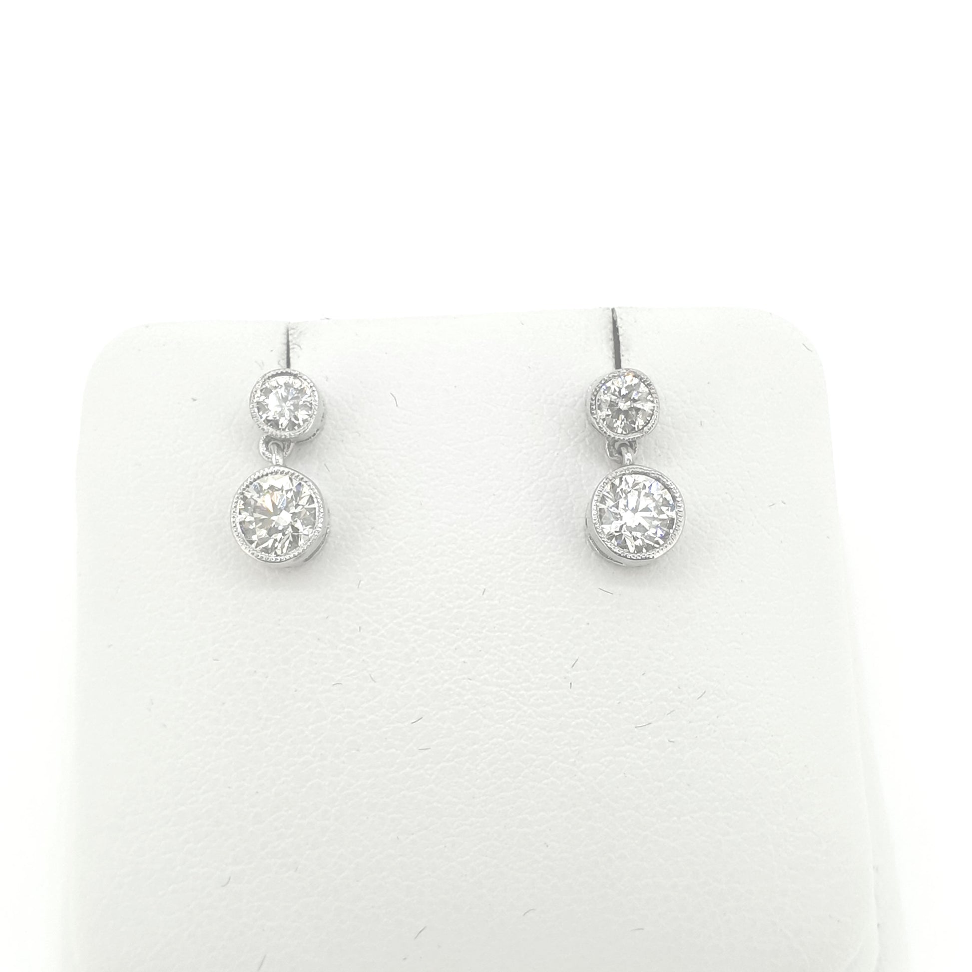 A pair of round brilliant cut diamond double drop earrings in white metal, on an earring display pad, on a white background