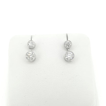 A pair of round brilliant cut diamond double drop earrings in white metal, on an earring display pad, on a white background