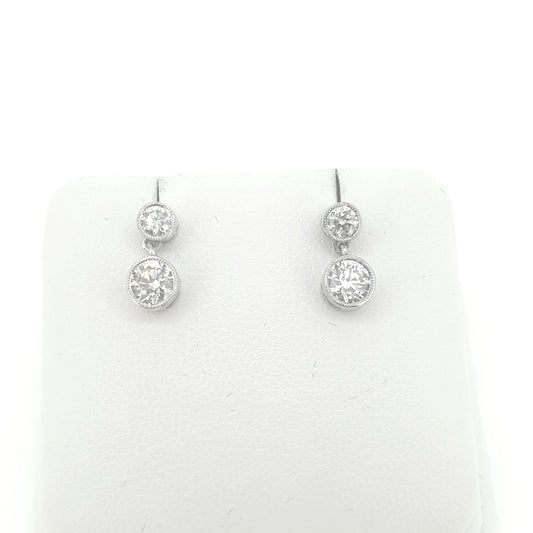A pair of round brilliant cut diamond double drop earrings in white metal, on an earring display pad, on a white background