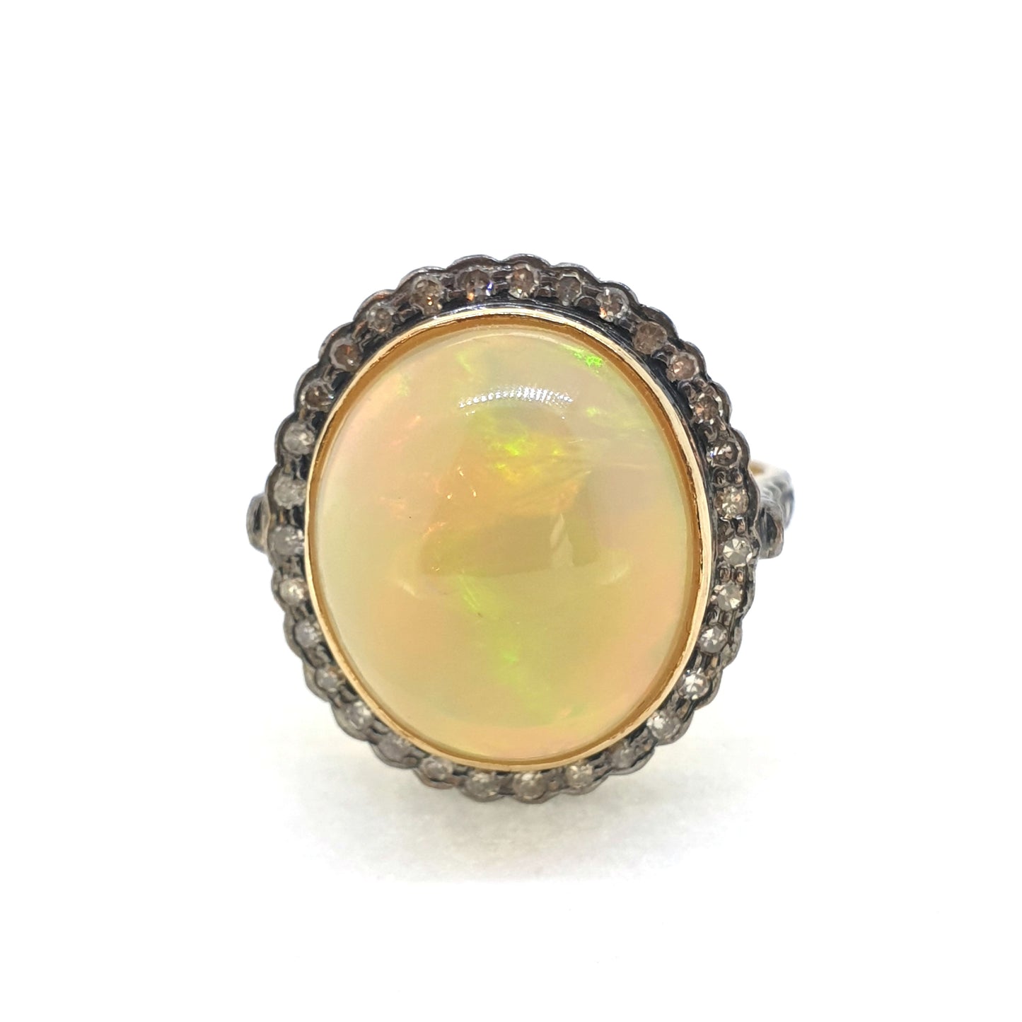 A cabochon opal and diamond oval cluster ring in gold and silver, on a white background