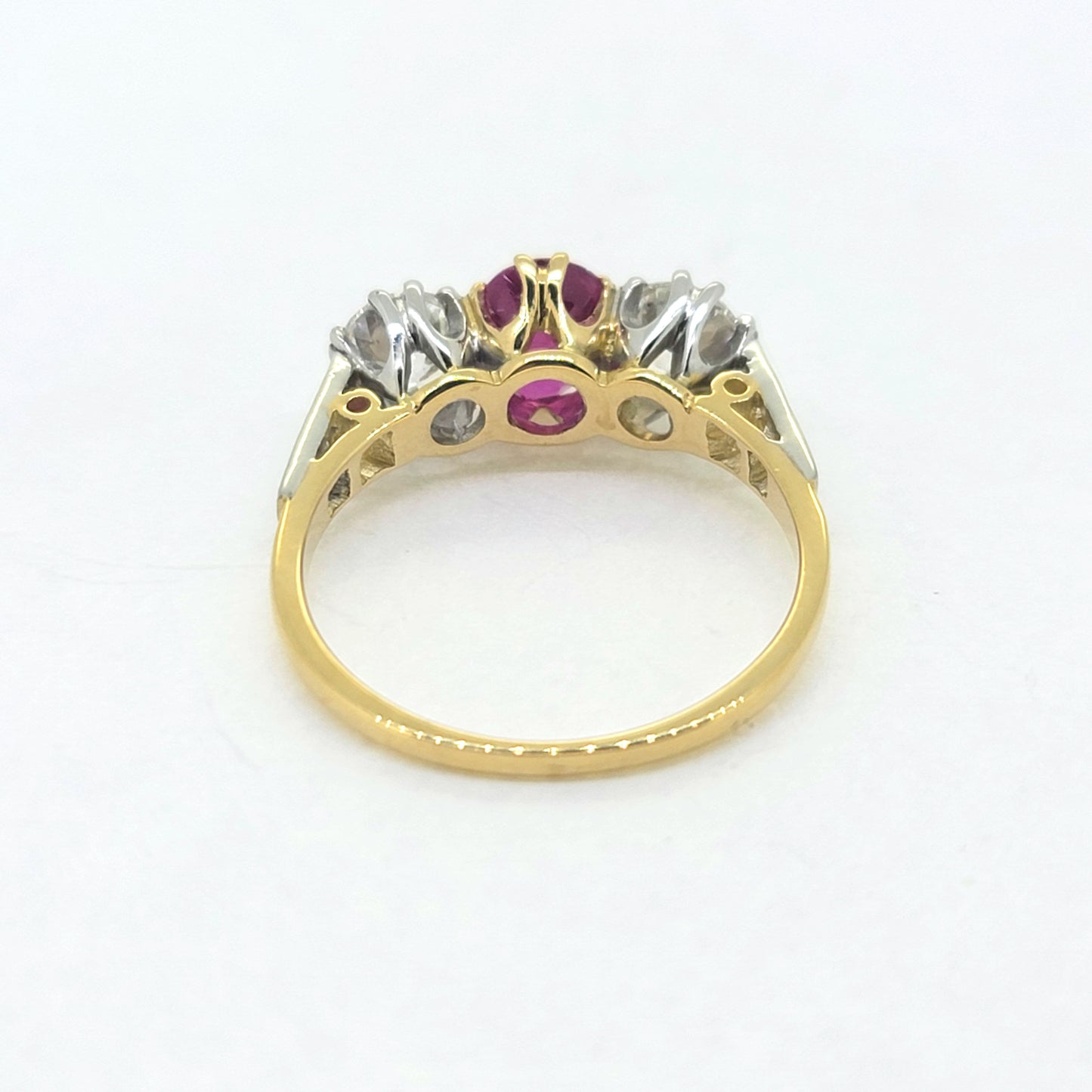 A three stone ruby and diamond ring in yellow and white gold, against a white background