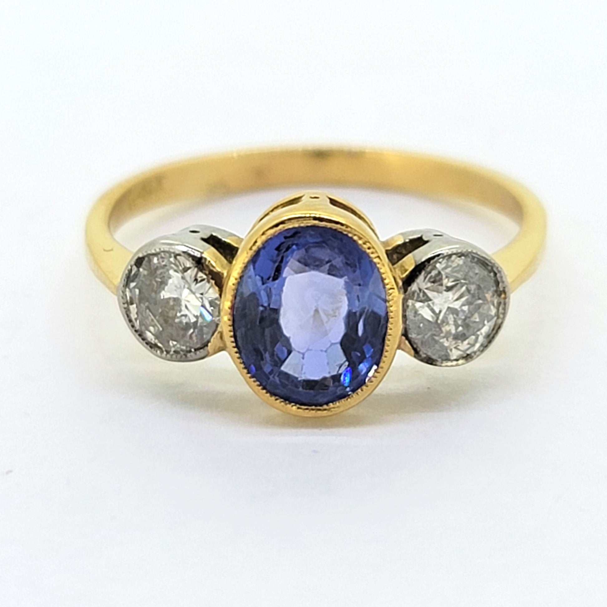 A three stone sapphire and diamond ring in yellow and white gold, on a white background