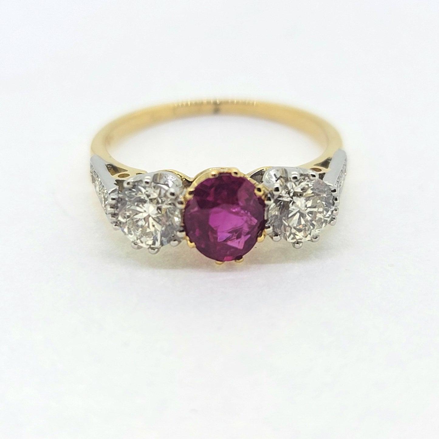 A three stone ruby and diamond ring in yellow and white gold, against a white background