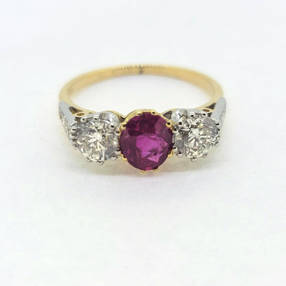 A three stone ruby and diamond ring in yellow and white gold, against a white background