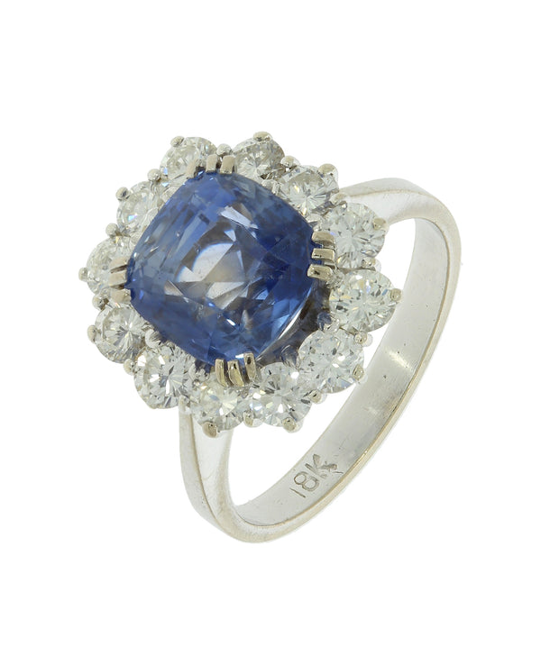 A white gold sapphire and brilliant cut diamond cluster ring, stamped 18K, on a white background