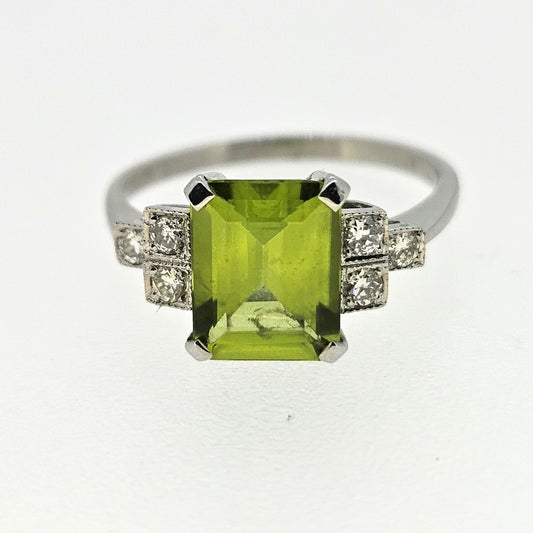 An emerald cut peridot ring with stepped diamond shoulders, in platinum