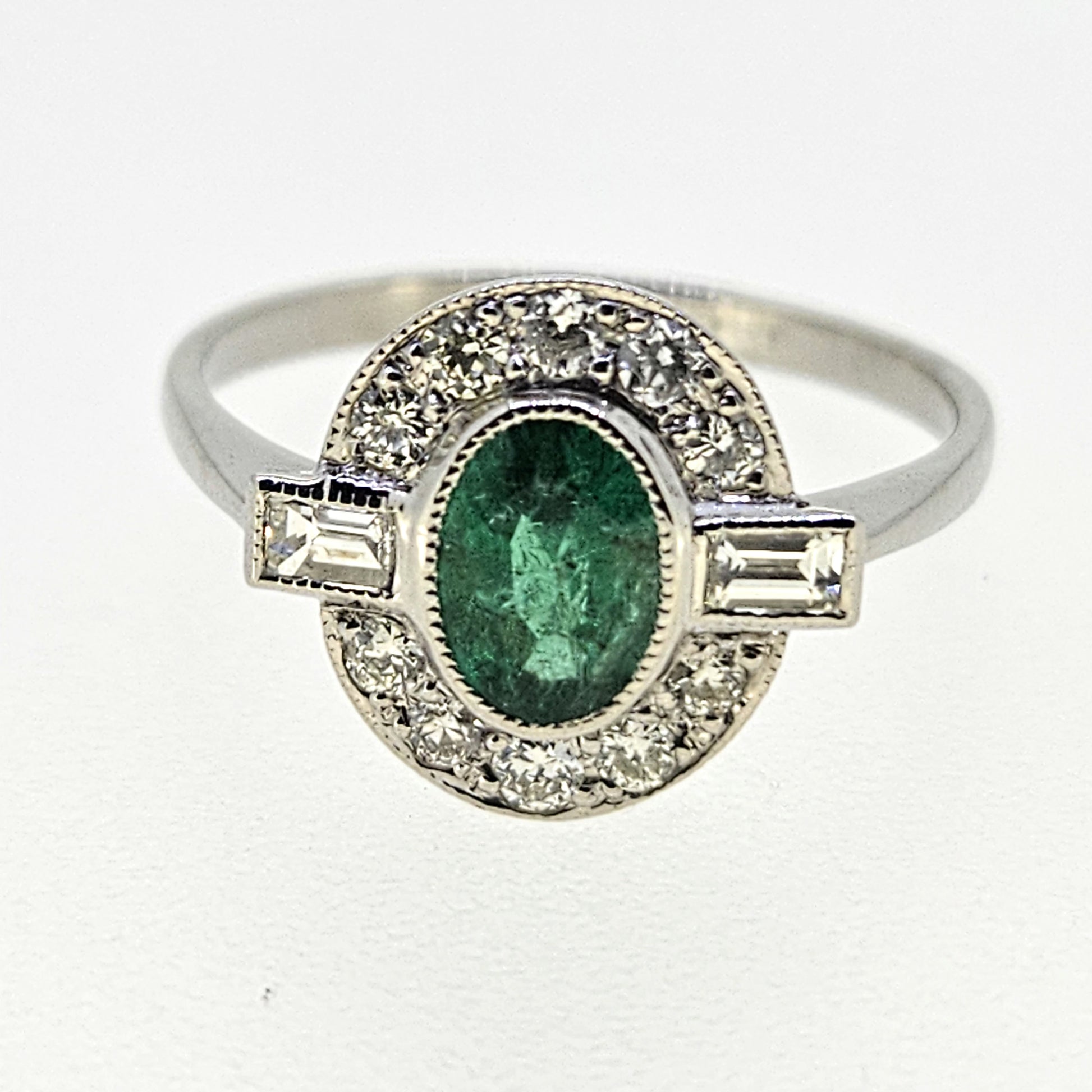 An oval emerald and diamond cluster ring in platinum