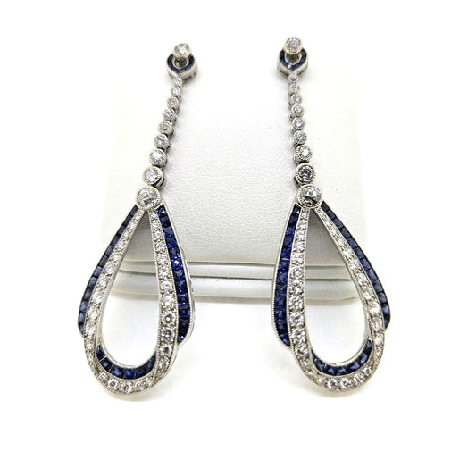 A pair of sapphire and diamond teardrop shaped long drop earrings in white gold, on an earring display pad, against a white background