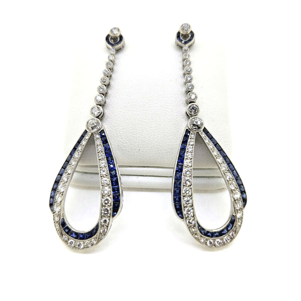 A pair of sapphire and diamond teardrop shaped long drop earrings in white gold, on an earring display pad, against a white background
