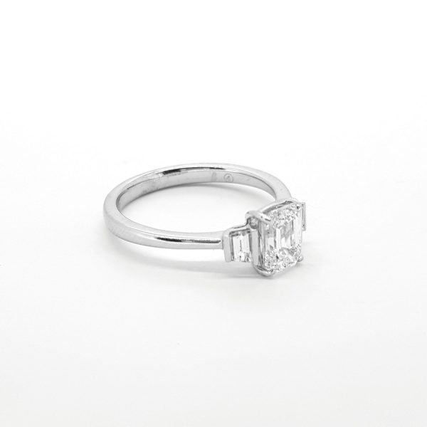 1ct Emerald Cut Diamond Ring with Baguette Shoulders; central claw set emerald-cut diamond accented with a channel-set baguette-cut diamond to each shoulder, in 18ct white gold
