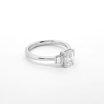 1ct Emerald Cut Diamond Ring with Baguette Shoulders; central claw set emerald-cut diamond accented with a channel-set baguette-cut diamond to each shoulder, in 18ct white gold