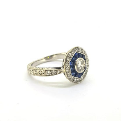 Vintage Sapphire and Diamond Cluster Target Ring, central brilliant-cut diamond surrounded by a hexagon of French cut sapphires and outer border of 18 brilliant cut pave set diamonds, in 18ct white gold with decorative engraving, Circa 1960