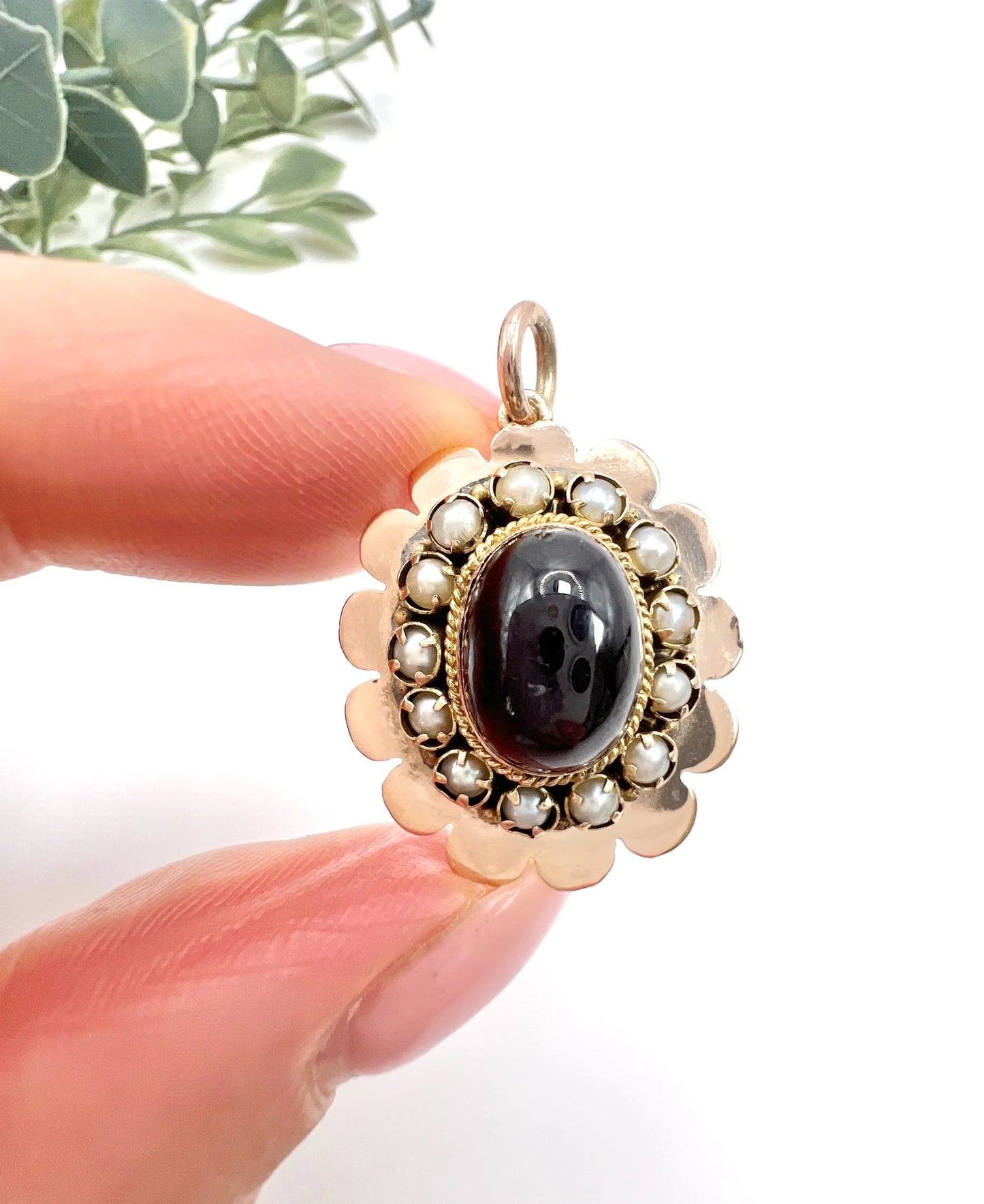 A cabochon garnet pendant with a seed pearl border in rose gold, held in a hand