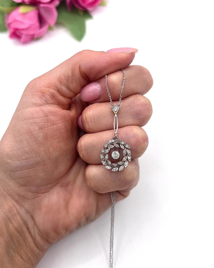A platinum floral wreath pendant with diamonds on a platinum chain, held in a hand