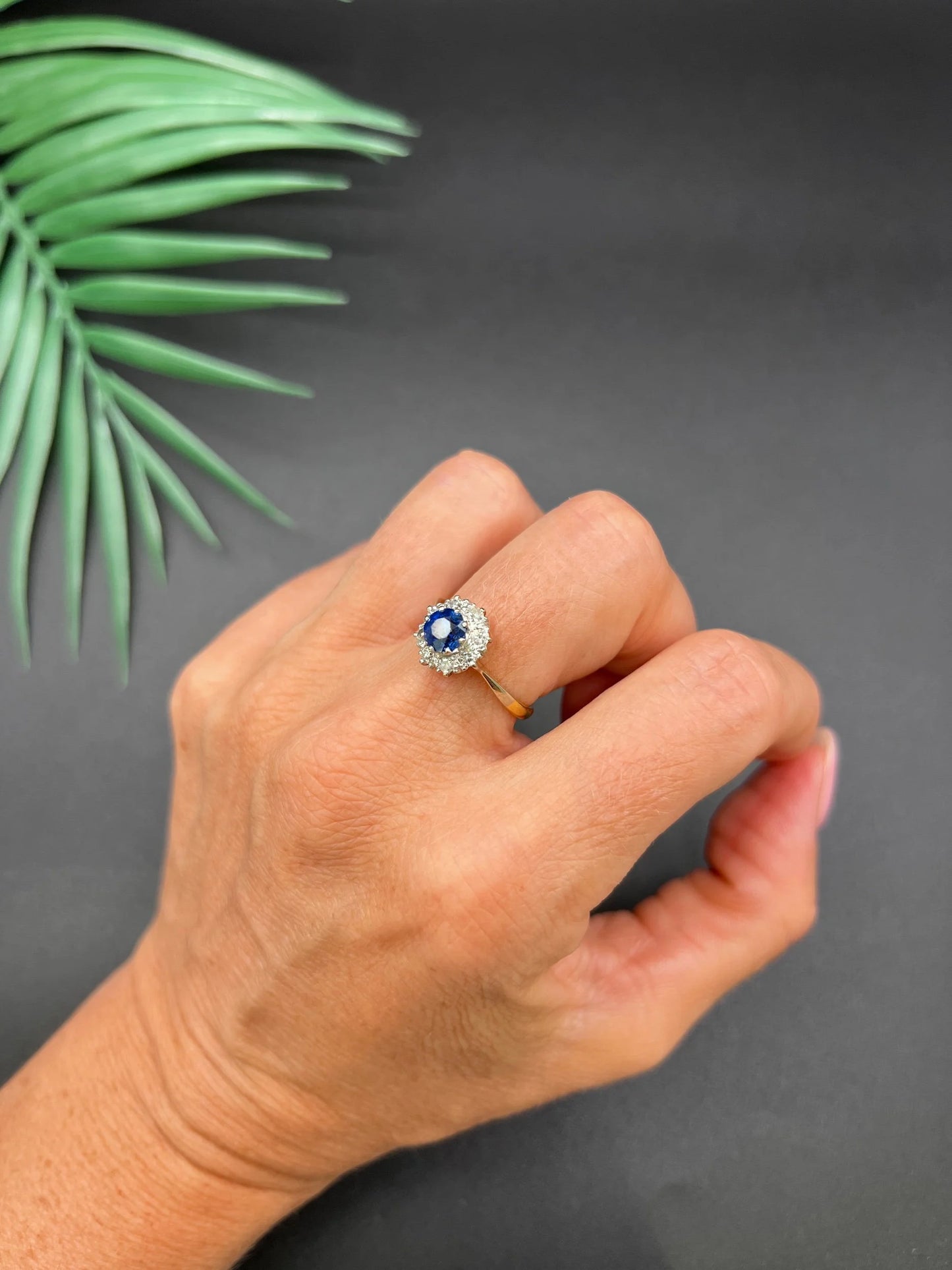 A circular cluster ring with sapphire and diamonds in yellow gold and platinum, modelled on a hand