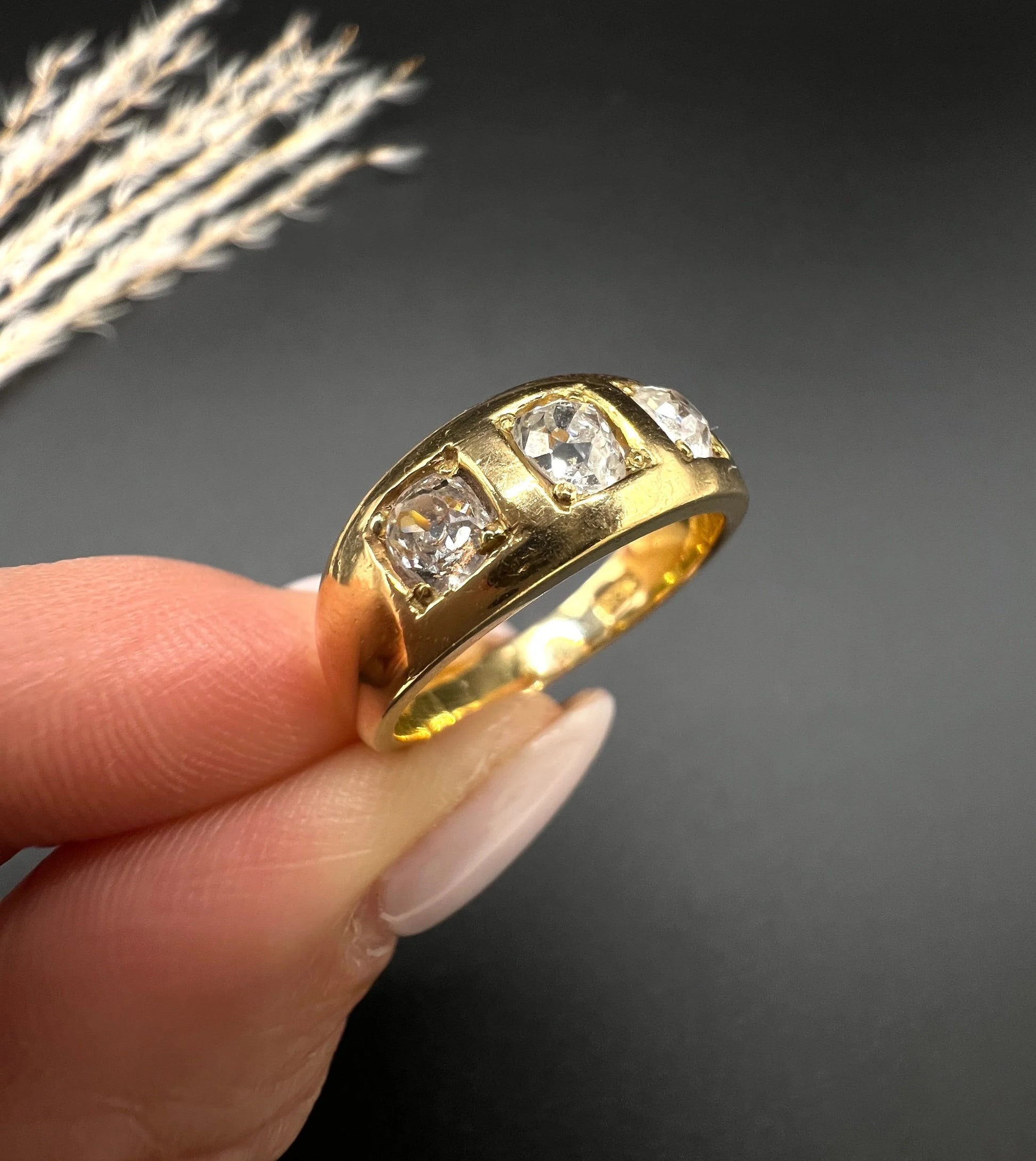 A three stone old cut diamond ring in yellow gold, held in a hand