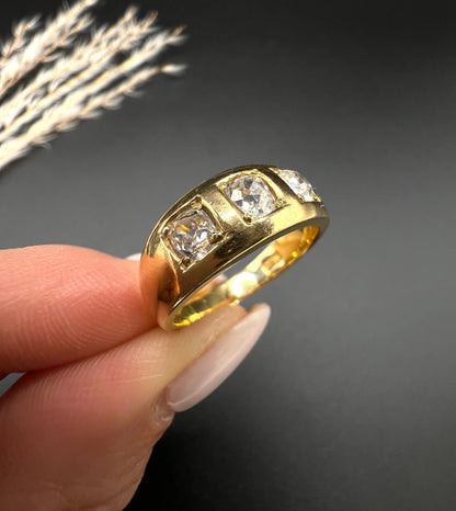 A three stone old cut diamond ring in yellow gold, held in a hand