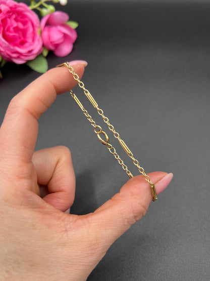 A yellow gold chain link bracelet with a bolt ring clasp, held in a hand