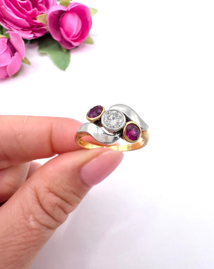 A three stone ruby and diamond crossover ring in platinum and yellow gold, held in a hand