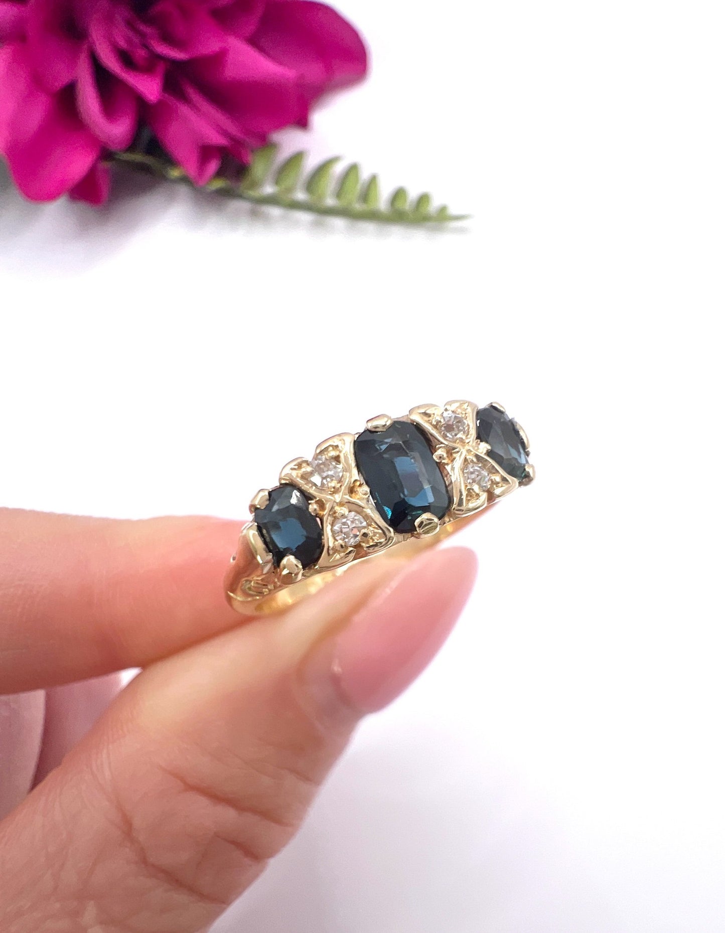 A seven stone sapphire and diamond carved ring in yellow gold, held in a hand