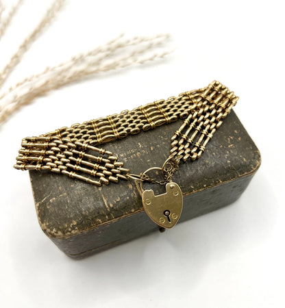 A yellow gold gate bracelet with heart shaped padlock clasp, on an antique bracelet box