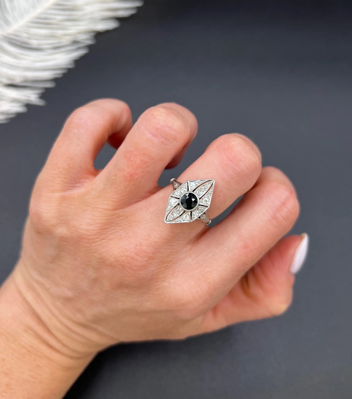A navette shaped cluster cocktail ring with a sapphire centre surrounded by diamonds, in platinum, modelled on a hand