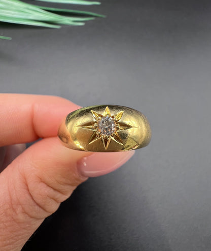 A single stone old cut diamond gypsy band ring in yellow gold, held in a hand