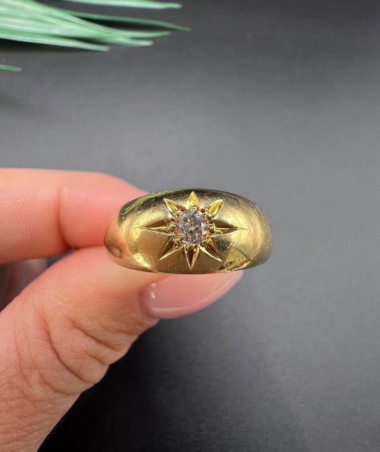 A single stone old cut diamond gypsy band ring in yellow gold, held in a hand