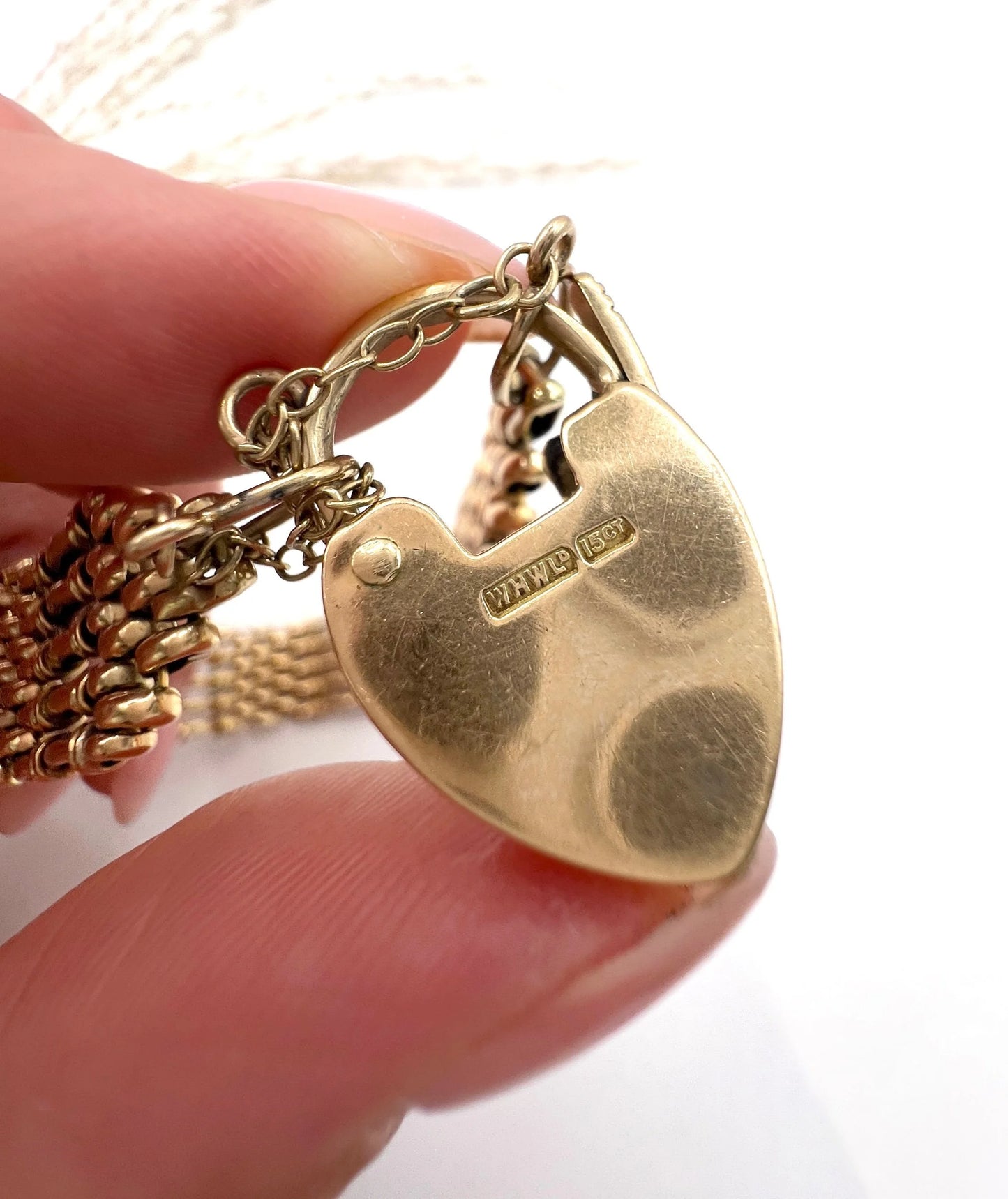 A close-up of a yellow gold heart shaped padlock, held in a hand