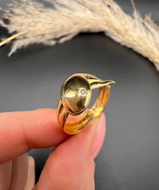 A yellow gold coiled snake ring with diamond eyes, held in a hand