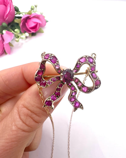 A ruby bow brooch necklace in gold and silver, held in a hand