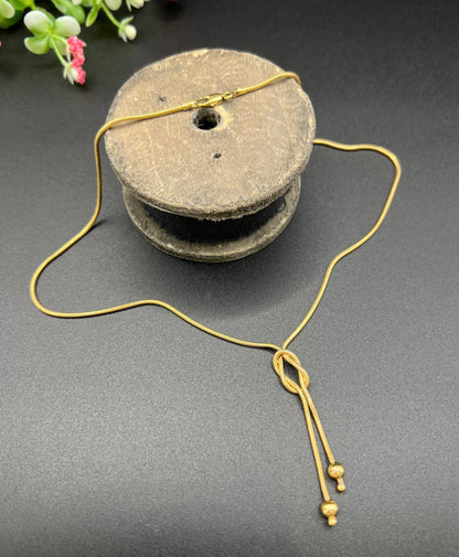 A yellow gold snake link chain necklace with a knot and tassel drop