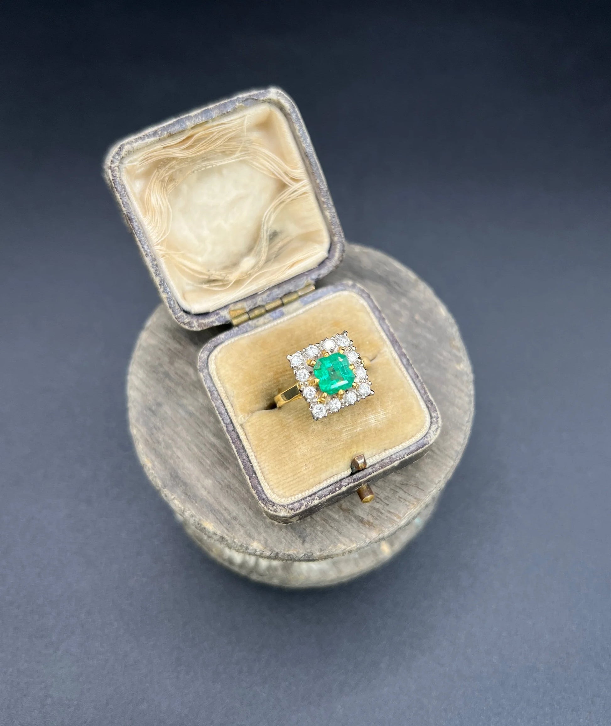 A square shaped emerald and diamond cluster ring in yellow and white gold, in a ring box
