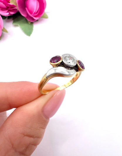 A three stone ruby and diamond crossover ring in platinum and yellow gold, held in a hand
