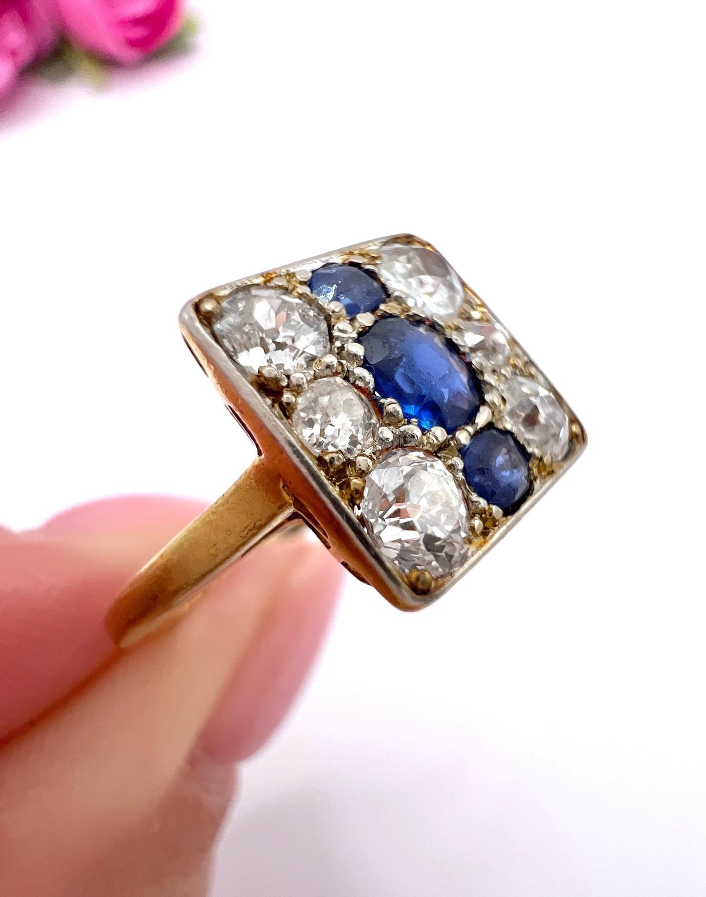 A square-shaped cluster ring with sapphires and diamonds in yellow gold and platinum, held in a hand